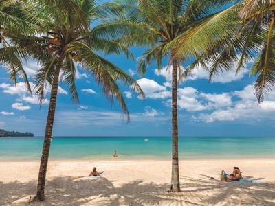 Strand mit Palmen, blauem Himmel und ruhigem Meer, Menschen entspannen auf dem Sand.