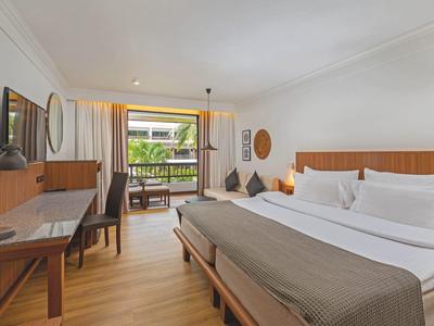 Modern eingerichtetes Hotelzimmer mit Doppelbett, Schreibtisch, Fernseher und Balkon mit Blick auf Grünfläche.