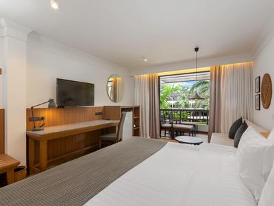 Modernes Hotelzimmer mit Doppelbett, Schreibtisch, Fernseher und Balkon mit grüner Außenansicht.