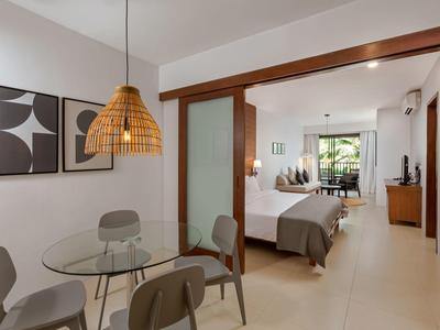 Moderner Essbereich mit runden Glastisch, grauen Stühlen und Blick ins Schlafzimmer mit Balkon.