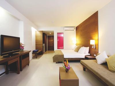 Modernes Hotelzimmer mit großem Bett, Sofa, Fernseher und hellen Wänden.