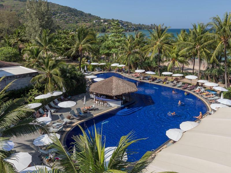 Großer Hotelpool mit Sonnenschirmen, Liegestühlen und Palmen in tropischer Umgebung.