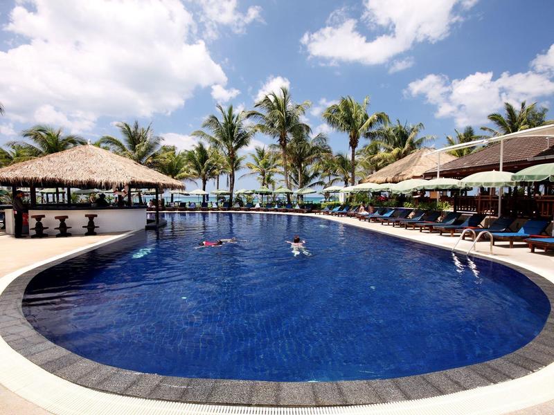 Großer Pool mit Sonnenschirmen und Palmen an einem sonnigen Tag im Resort.