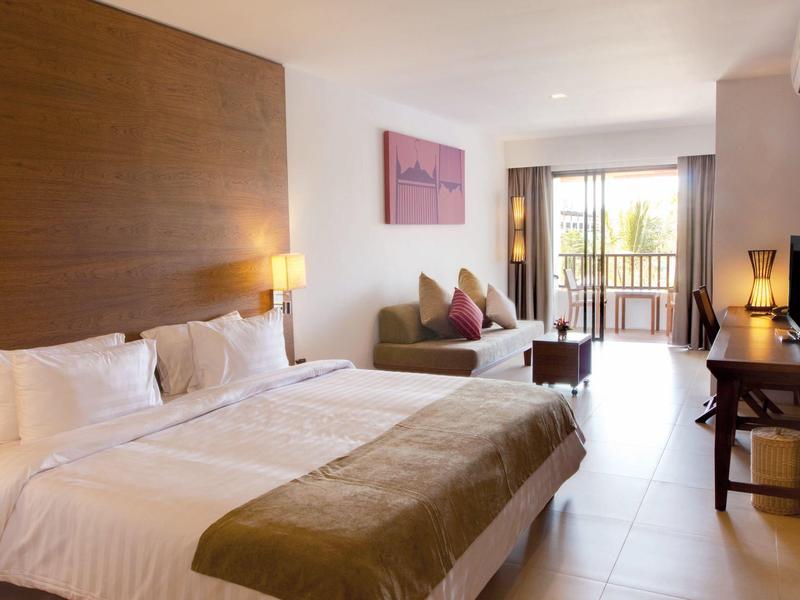 Helles Hotelzimmer mit Doppelbett, Sofa, Schreibtisch und Balkon mit Blick ins Grüne.