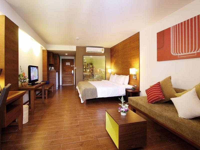 Modern eingerichtetes Hotelzimmer mit Doppelbett, Sofa und Fernseher auf Holzfußboden.