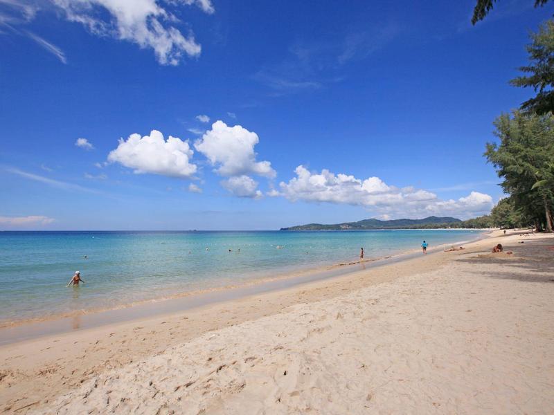 Wide sandy beach with clear water under a blue sky with some clouds.