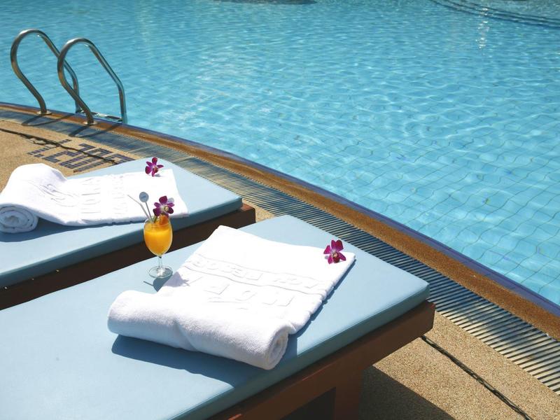 Two lounge chairs with white towels and drinks by a hotel poolside.