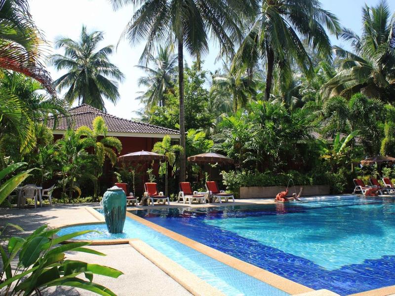 Schwimmbecken umgeben von Palmen und Liegestühlen mit Menschen im tropischen Garten.