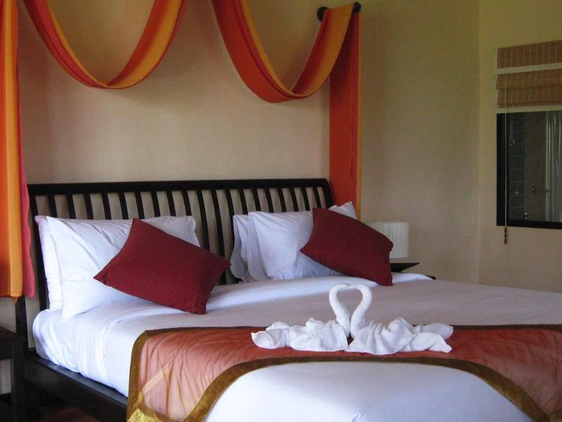 Gemütliches Schlafzimmer mit weißem Bett, roten Kissen, orange-roter Wanddeko und Schwanenhandtüchern.