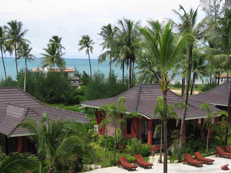 Tropische Bungalows mit roten Dächern, Palmen und Blick auf türkisblaues Meer.