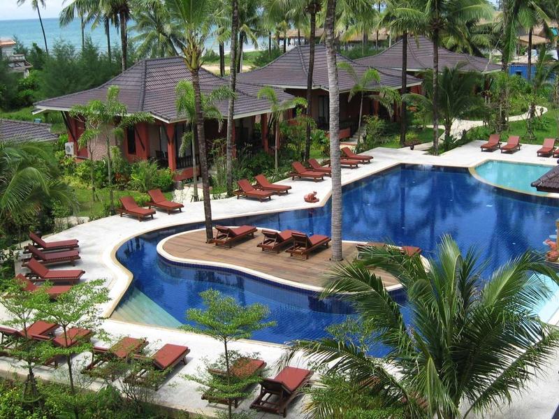 Große Poolanlage in tropischer Gartenanlage mit Palmen, Liegestühlen und Holzdecks.