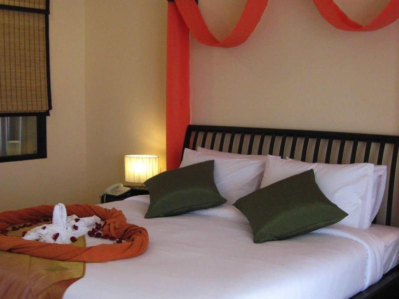 Schlafzimmer mit Doppelbett, weißen Laken, grünen Kissen, braunen Decken und weicher Beleuchtung.