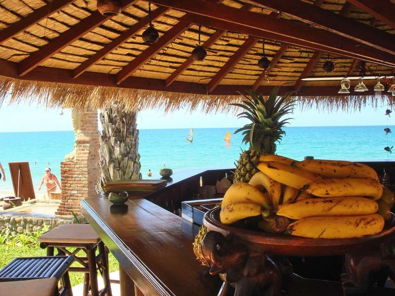 Offene Strandbar mit tropischem Holzdach, Fruchtkorb mit Bananen und Ananas am Naturholz-Tresen.