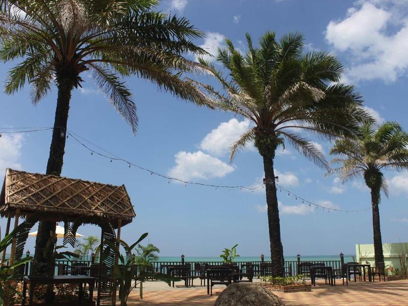 Strand mit Palmen, Holzhütte und klarem Himmel über ruhigem Meer im Hintergrund.
