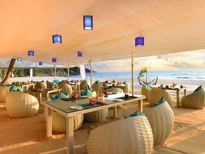 Offener Strandrestaurantbereich mit weißen Möbeln und Blick auf das Meer bei Sonnenuntergang.