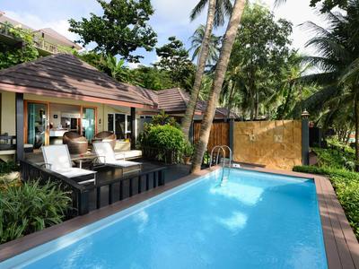 Modern pool with lounge furniture beside tropical garden and bungalow.