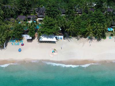 Aerial view of a tropical beach with white sand, turquoise sea, and palm-lined buildings.