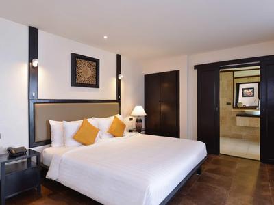Modern hotel room with large double bed, white and orange pillows, and minimalist decor.