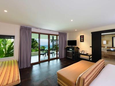 Hotel room with balcony view and tropical plants, modern interior with bed and sofa.