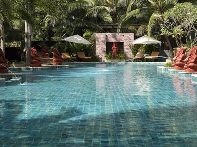 Ein klarer blauer Pool umgeben von grünen Bäumen und roten Statuen in einem tropischen Hotel.