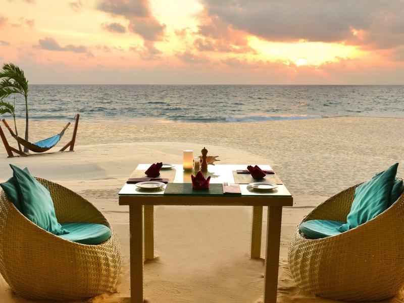 Table with breakfast and two chairs on the beach at sunrise with hammock in the background.