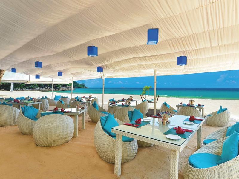 Beach restaurant with white and blue furniture under a white fabric canopy on sandy shore.