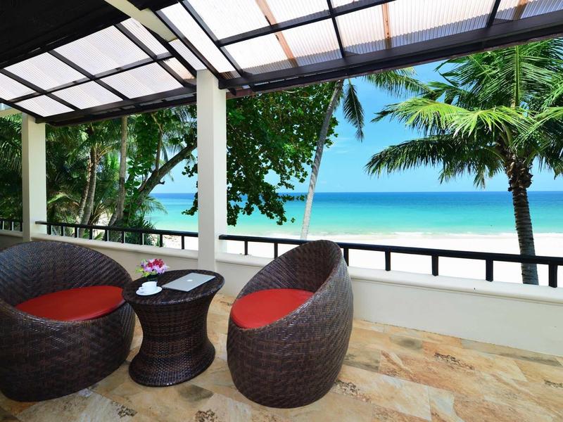 Terrace with two round chairs and table overlooking tropical beach and sea.