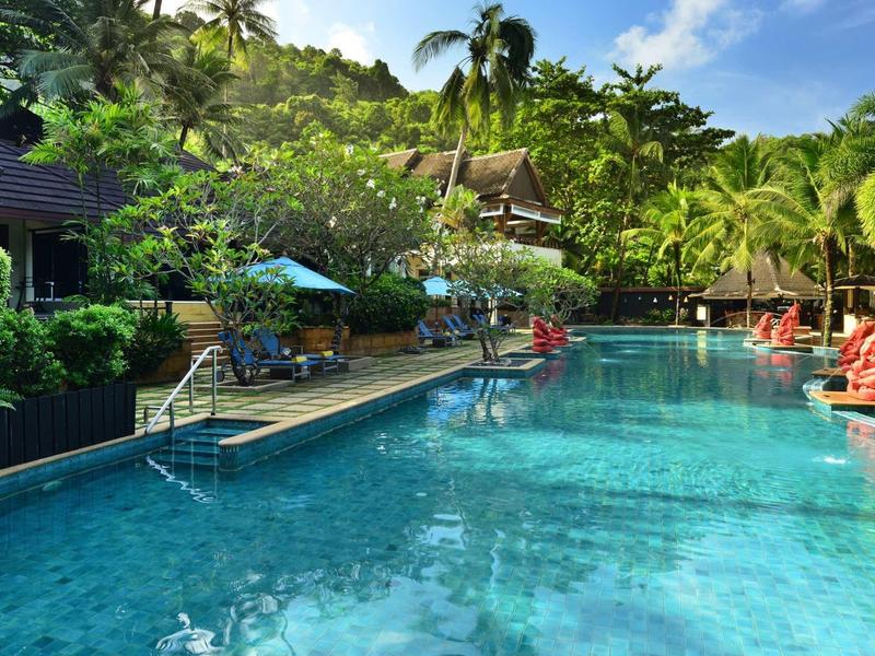 Clear water pool in tropical hotel setting surrounded by palm trees and sun umbrellas.