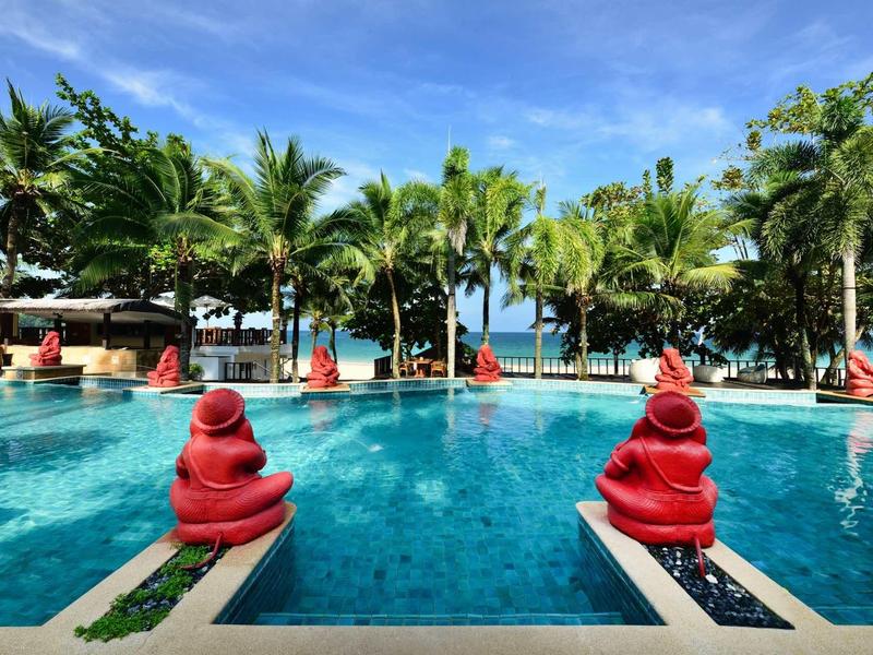 Clear water pool surrounded by palm trees and red decorations at a tropical resort.