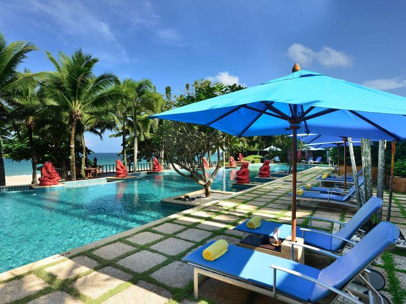 Pool area with blue loungers and umbrellas, tropical palms and sea in the background