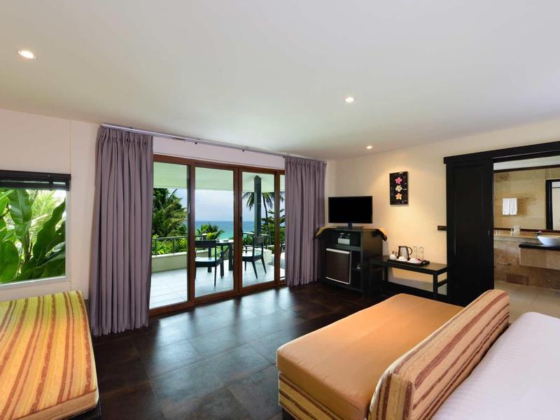 Hotel room with balcony view and tropical plants, modern interior with bed and sofa.