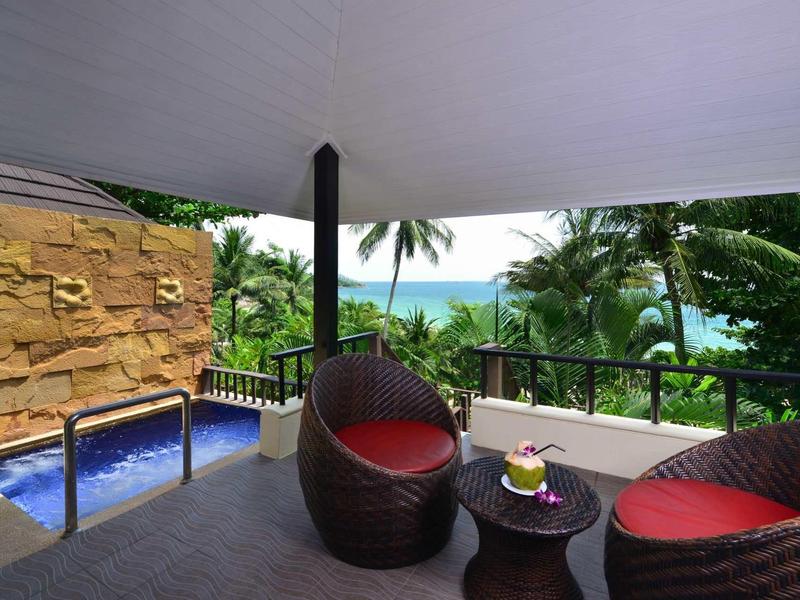 Balcony with modern rattan chairs, small table, and pool overlooking tropical vegetation.