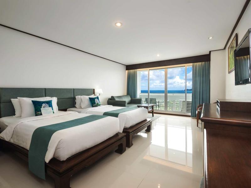 Modernes Hotelzimmer mit zwei großen Betten, TV, Fenster mit Meerblick und hellen Fliesenböden.