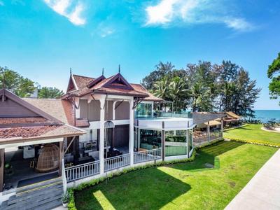 Großes Haus mit Balkonen und Glasgeländer, umgeben von grünem Rasen und Blick aufs Wasser.