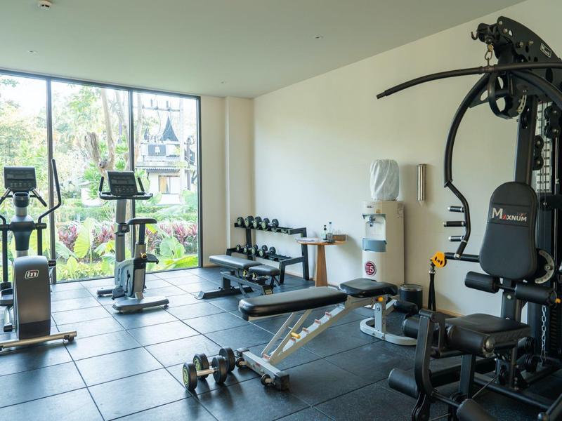 Moderner Fitnessraum mit Geräten, Hanteln und großen Fenstern für viel Tageslicht.