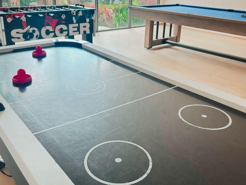 Moderner Airhockey-Tisch in schwarz-weiß mit roten Schlägern in einem Raum mit Fußballspiel und Billardtisch.