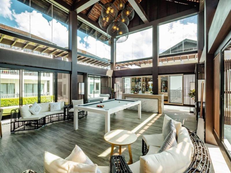 Helles, modernes Wohnzimmer mit hohen Decken, großen Fenstern, Sitzgruppen und einem Billardtisch.