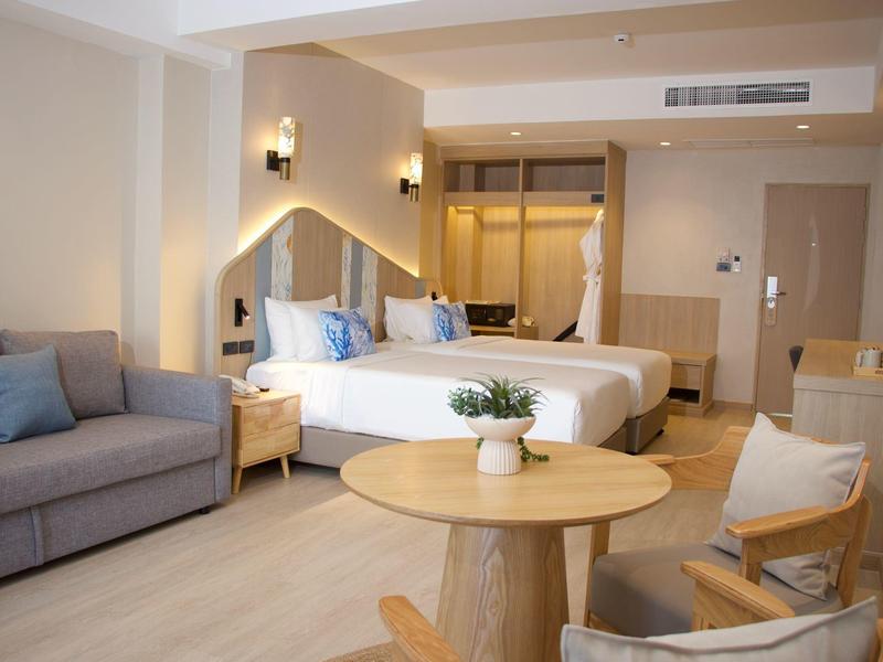 Modern eingerichtetes Hotelzimmer mit Doppelbett, Sofa, rundem Holztisch und zwei Stühlen.