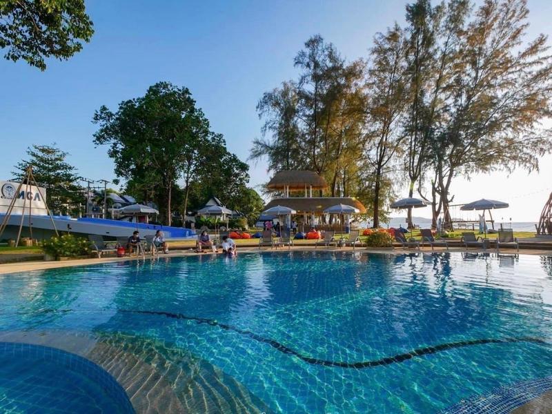 Großer Pool vor einem Hotel mit Sonnenschirmen und Bäumen bei Sonnenuntergang.