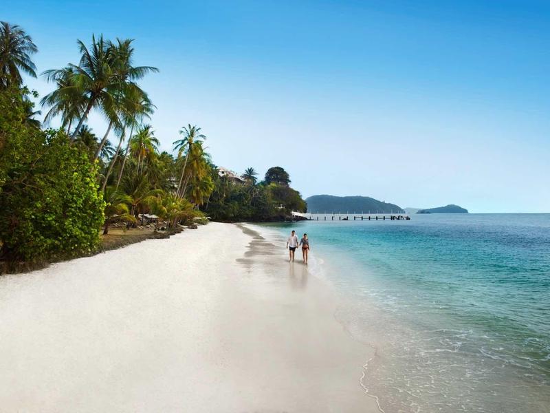 Strand mit weißem Sand, Palmen und klarem blauen Wasser unter sonnigem Himmel.