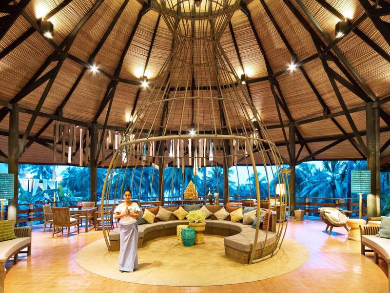 Großer, runder Innenraum mit Holzdeckendach, gemütlichen Sitzgruppen und einer begrünten Außenansicht.