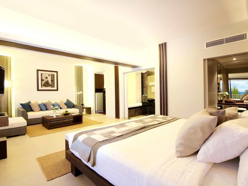 Modernes Hotelzimmer mit großem Bett, Sofa, TV und großen Fenstern für Tageslicht.