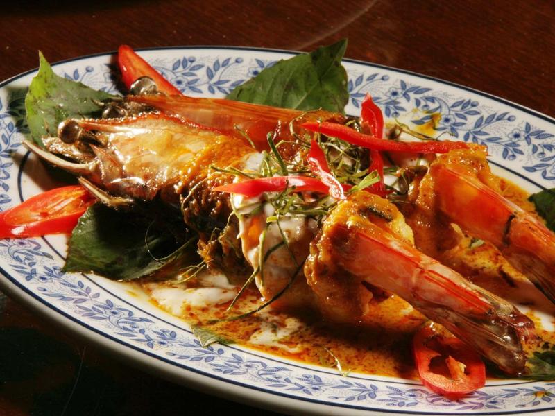 Gegrillte Garnelen mit rotem Chili und Kräutern auf weiß-blauem dekorativem Teller mit Blattsalat.