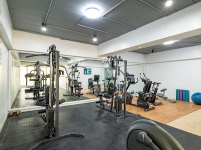 Moderner Fitnessraum mit Gewichten, Geräten und Spiegeln in einem Hotel.
