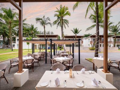 Outdoor-Restaurantbereich mit gedeckten Tischen und Blick auf Palmen und Hotelgebäude.