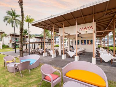 Offener Außenbereich einer Hotelbar mit Sitzgelegenheiten und Palmen bei Sonnenuntergang.