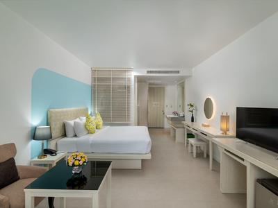 Modernes Hotelzimmer mit Doppelbett, Sitzbereich, Fernseher und Schreibtisch in neutralen Farben.