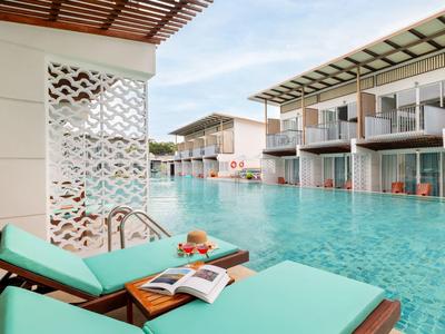 Moderne Hotelanlage mit Pool und Liegestühlen auf der Terrasse, darunter ein Buch und Obst.