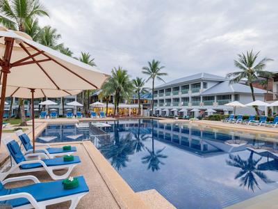 Moderner Hotelpool mit blauen Liegestühlen und Sonnenschirmen unter bewölktem Himmel.