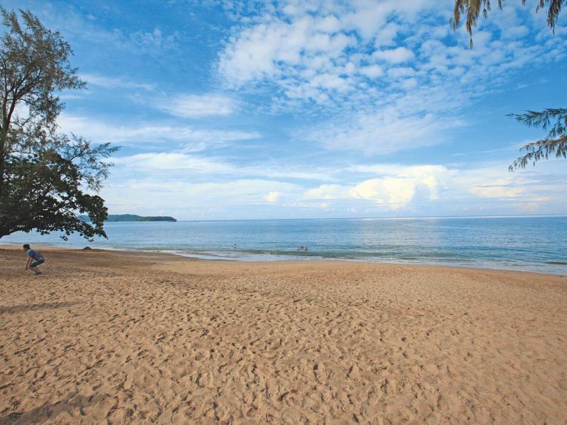 Weiter Sandstrand mit Bäumen und ruhigem Meer unter bewölktem Himmel
